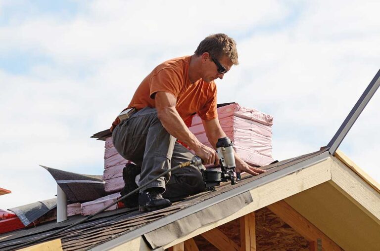 Worker examines a tarp-covered roof while a homeowner observes from the ground during a light snowfall.