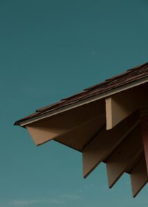 Close view of a sloped roof eave with soffit vents, fascia, gutter, and rainwater flowing into a downspout