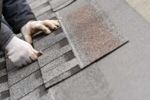 Homeowner examining curled shingles, rusted flashing, and roof granules beside a ladder after winter weather.